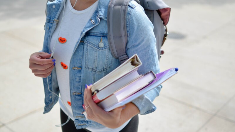 Tjej går med ryggsäck och böcker i famnen på gymnasial nivå