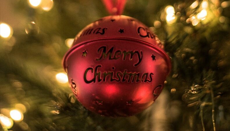 Röd julkula som hänger i en upplyst gran, med texten; Merry Christmas - God Jul, på Hultsfred Lärcenter